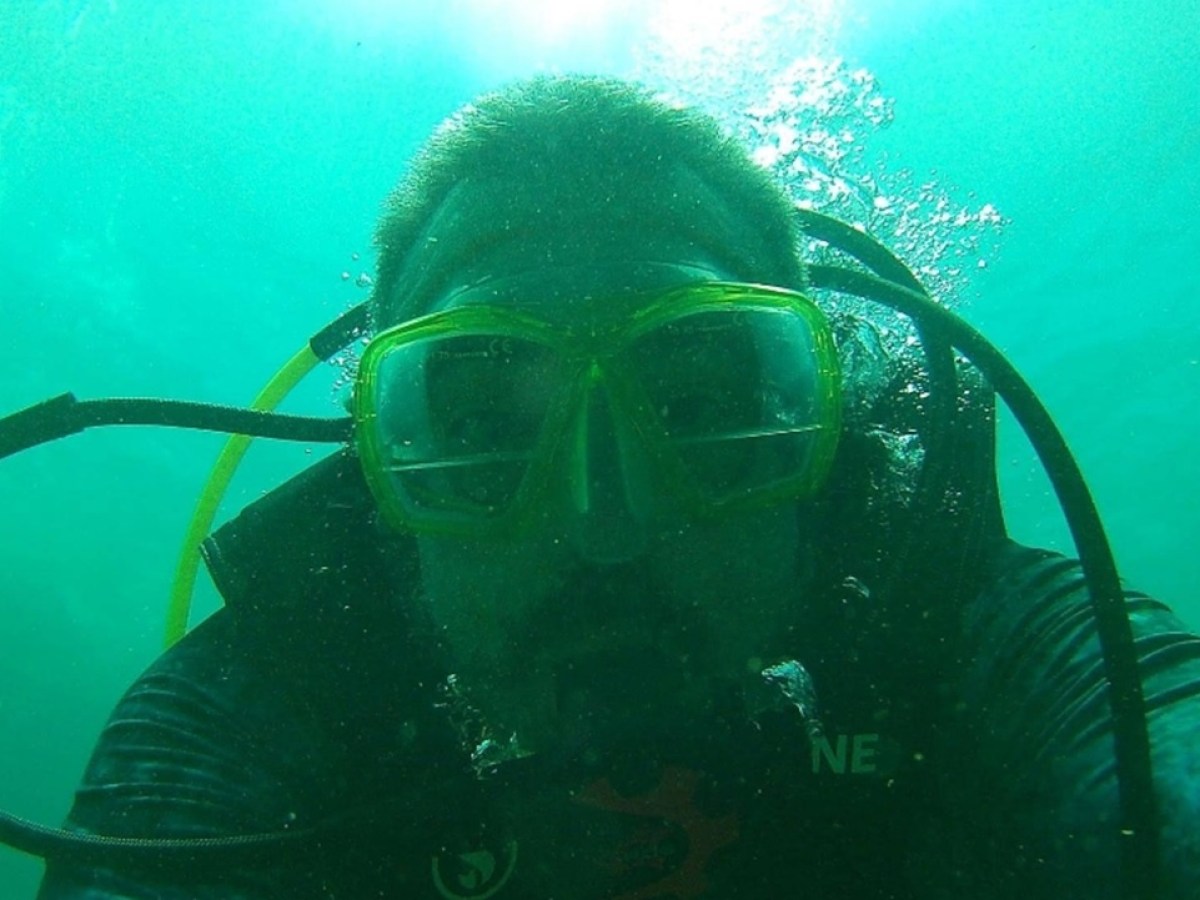 Diver underwater wearing a mask and scuba gear, surrounded by green water.