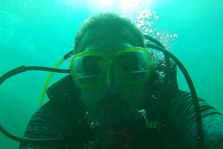 Diver underwater wearing a mask and scuba gear, surrounded by green water.