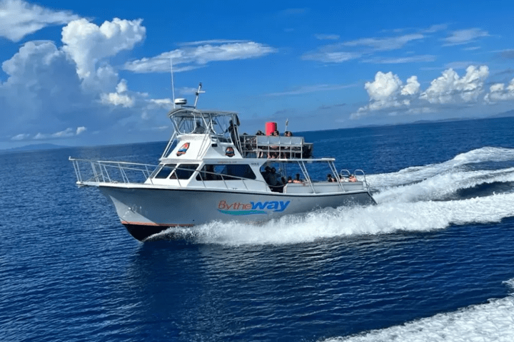 A white boat cruising in the ocean under a clear blue sky with scattered clouds.
