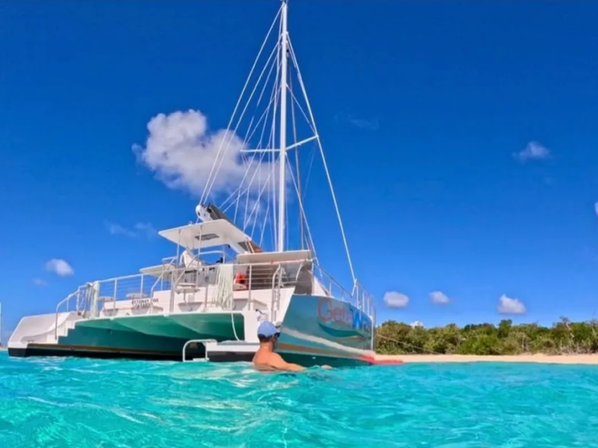 Person swimming near a sailboat on clear turquoise water under blue sky.