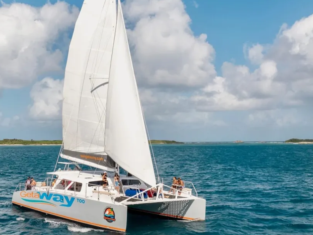 White catamaran sailing on the ocean under a partly cloudy sky with people on board.