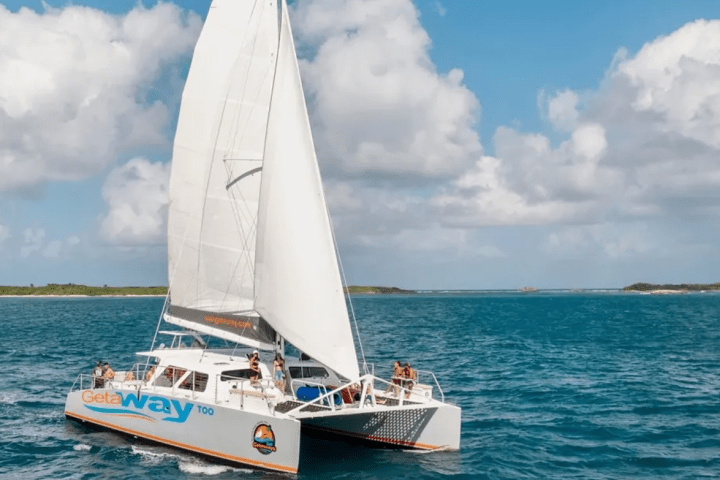 White catamaran sailing on the ocean under a partly cloudy sky with people on board.
