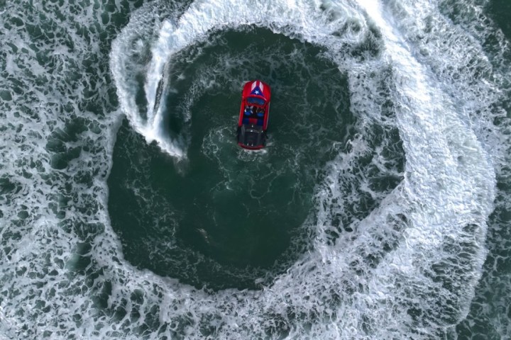 Aerial view of a red speedboat making a circular wake in the ocean.