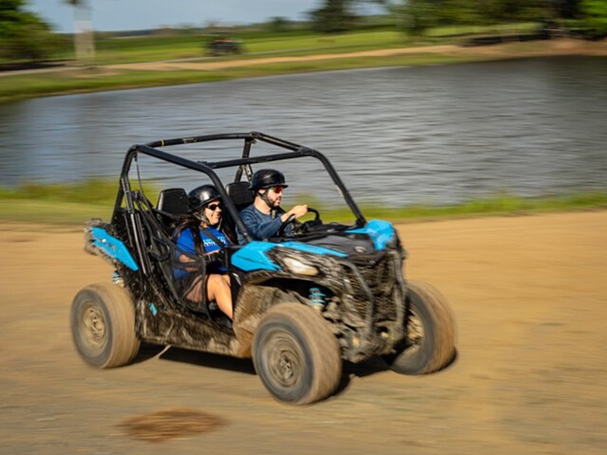 Two people in helmets driving a blue off-road vehicle by a lake.