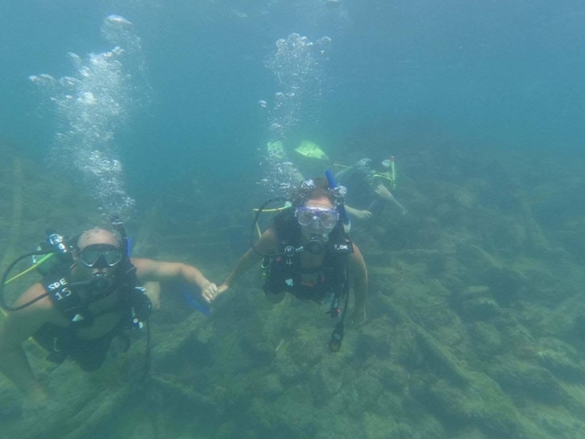 Two scuba divers underwater holding hands with another diver in the background.