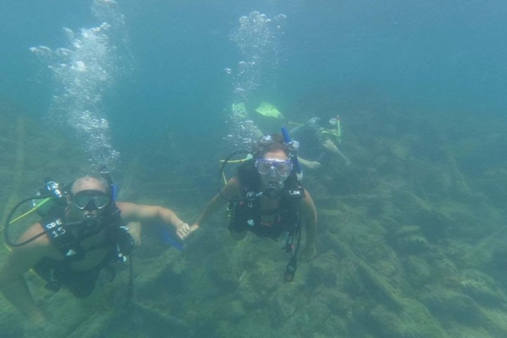 Two scuba divers underwater holding hands with another diver in the background.
