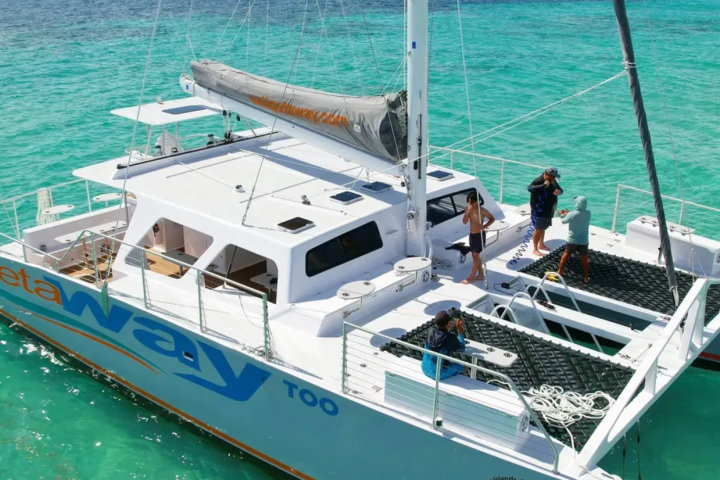 People on a white catamaran in clear turquoise water, with a visible sail.