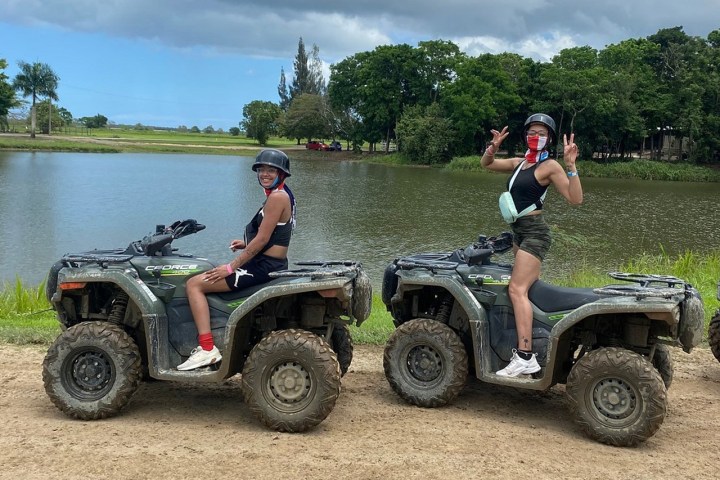 Two people on ATVs near a lake, posing with peace signs under a cloudy sky.
