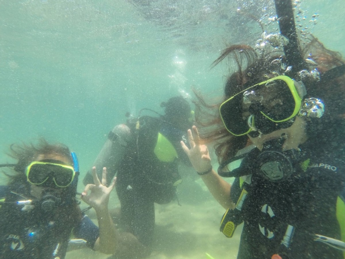 Three scuba divers underwater making OK hand signals.
