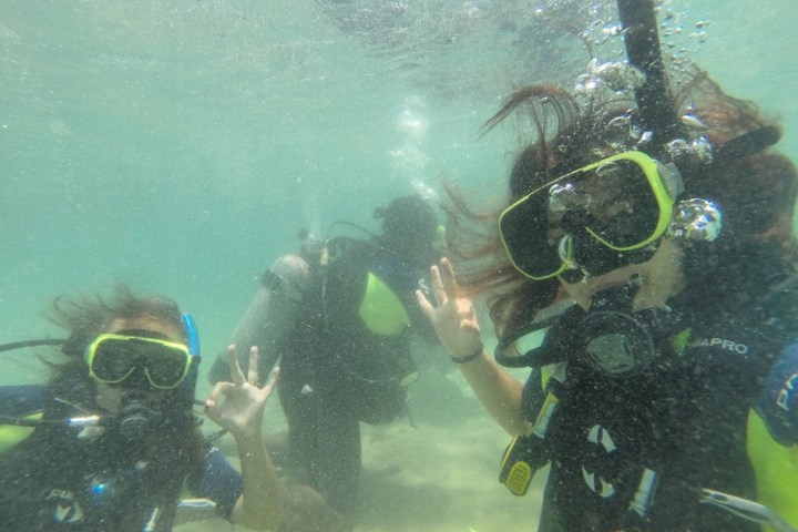 Three scuba divers underwater making OK hand signals.