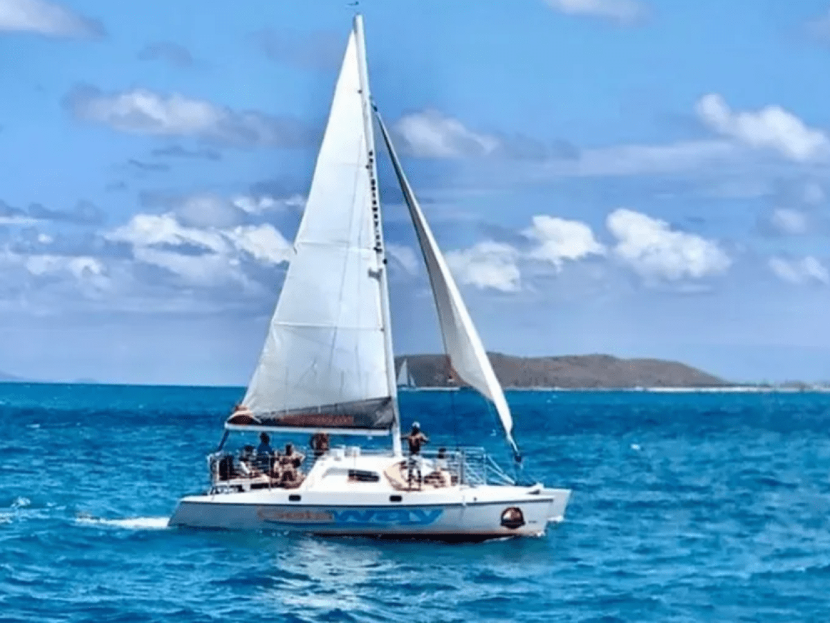 Sailboat with people on turquoise sea under blue sky with clouds.