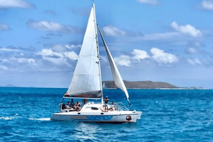 Sailboat with people on turquoise sea under blue sky with clouds.