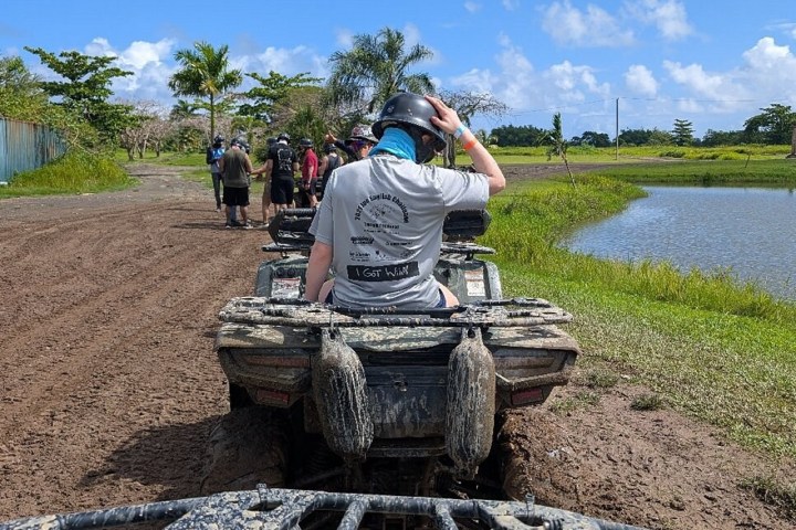 Person on an ATV wearing a helmet, with a muddy path and small lake in the background.