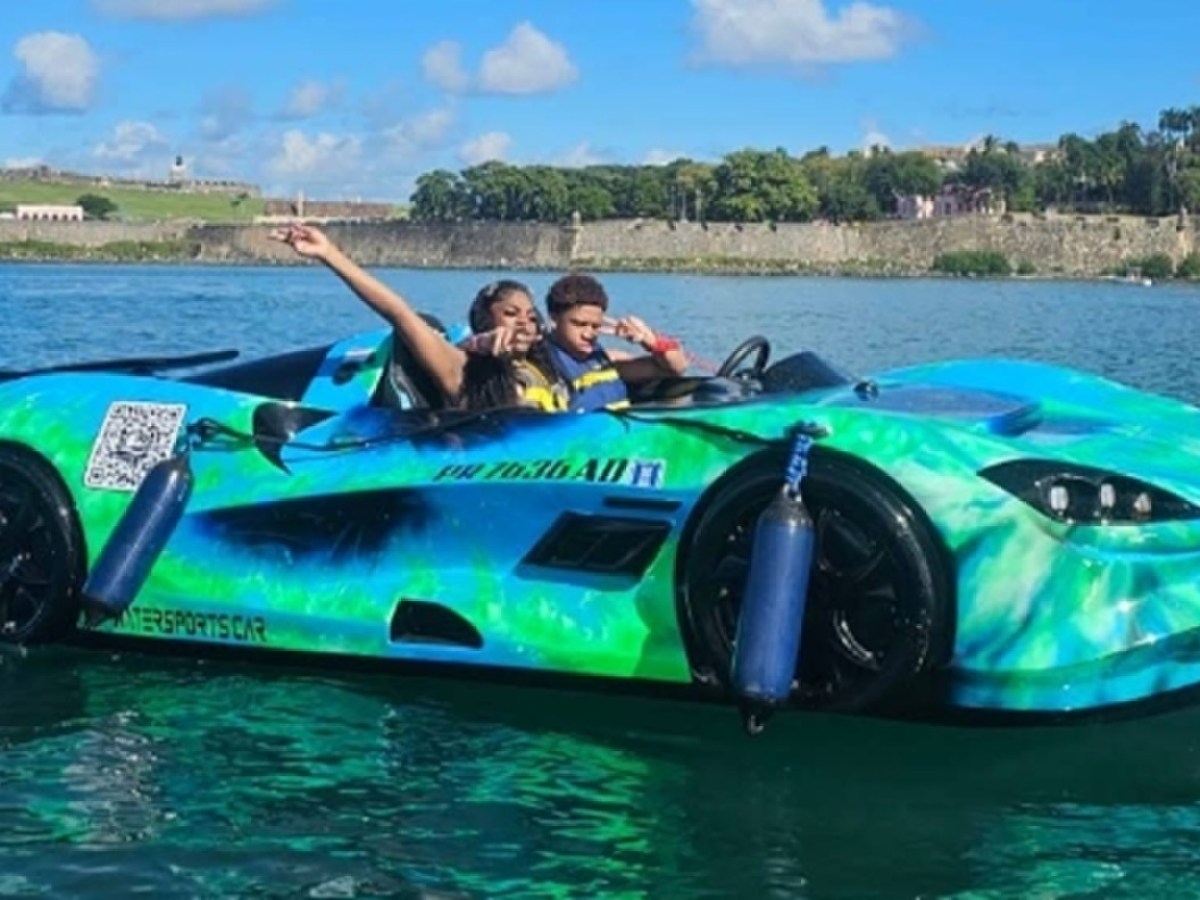 Two people in a colorful sports car shaped boat on water, with a scenic background.