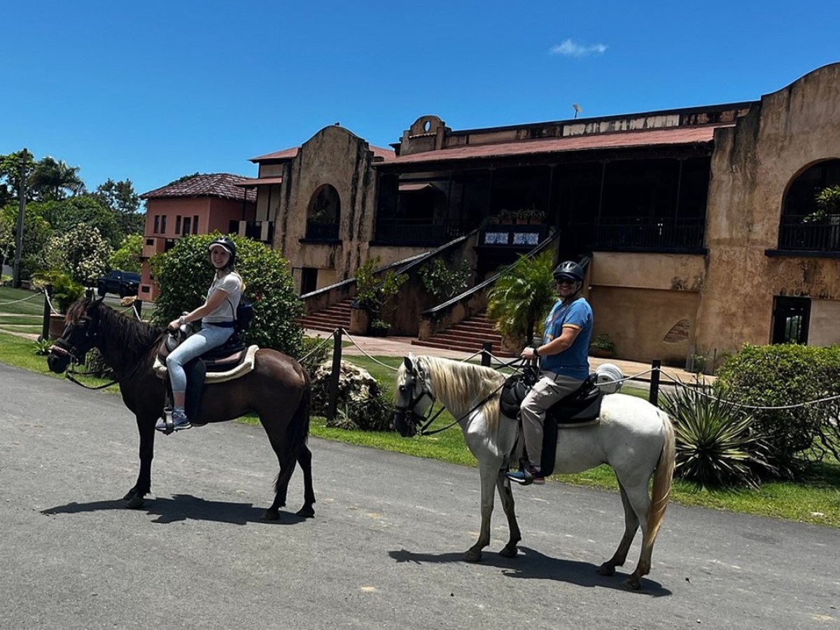 Two people riding horses in front of an old building on a sunny day.