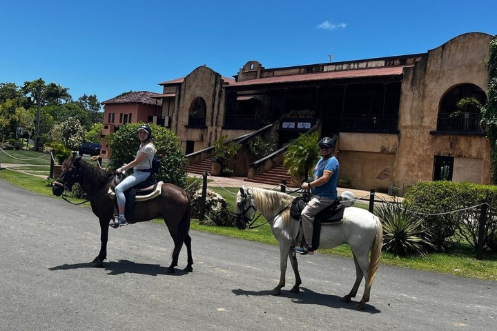 Two people riding horses in front of an old building on a sunny day.