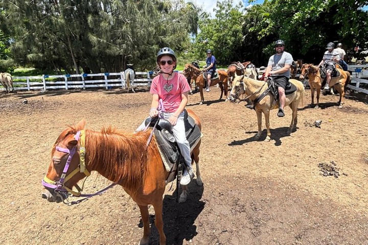 Group of people horseback riding in a sunny paddock, wearing helmets.