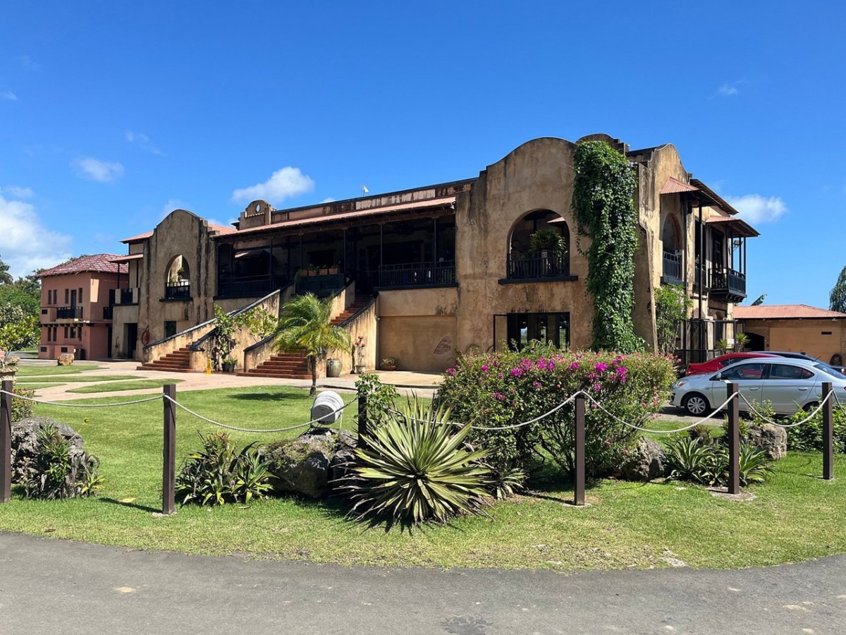 Rustic building with arched windows, surrounded by greenery under a clear blue sky.