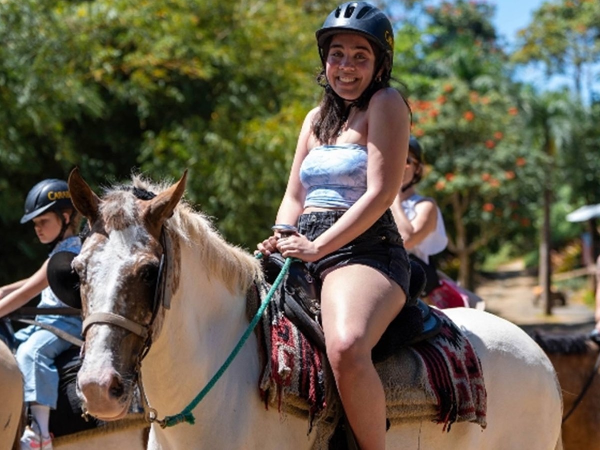 Smiling woman in helmet horseback riding outdoors on a sunny day.