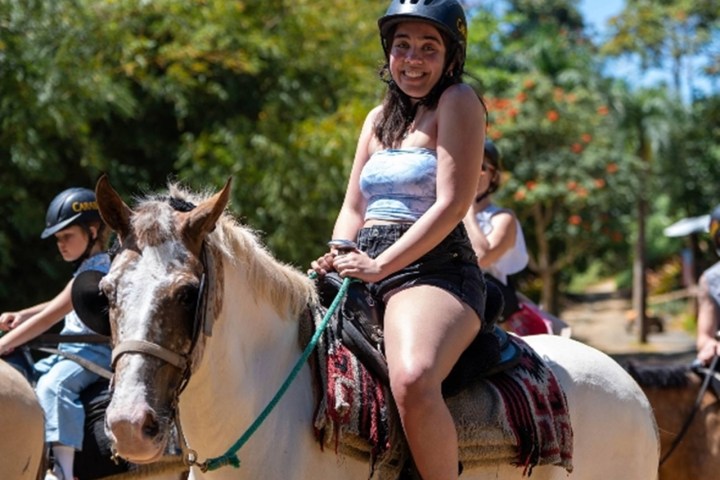 Smiling woman in helmet horseback riding outdoors on a sunny day.