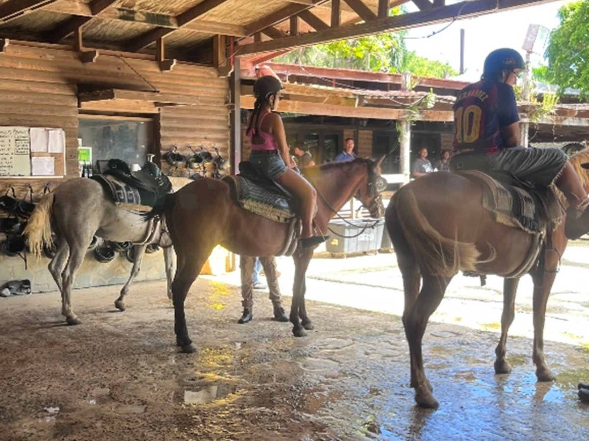 Two people on horses inside a wooden stable, facing away from the camera.