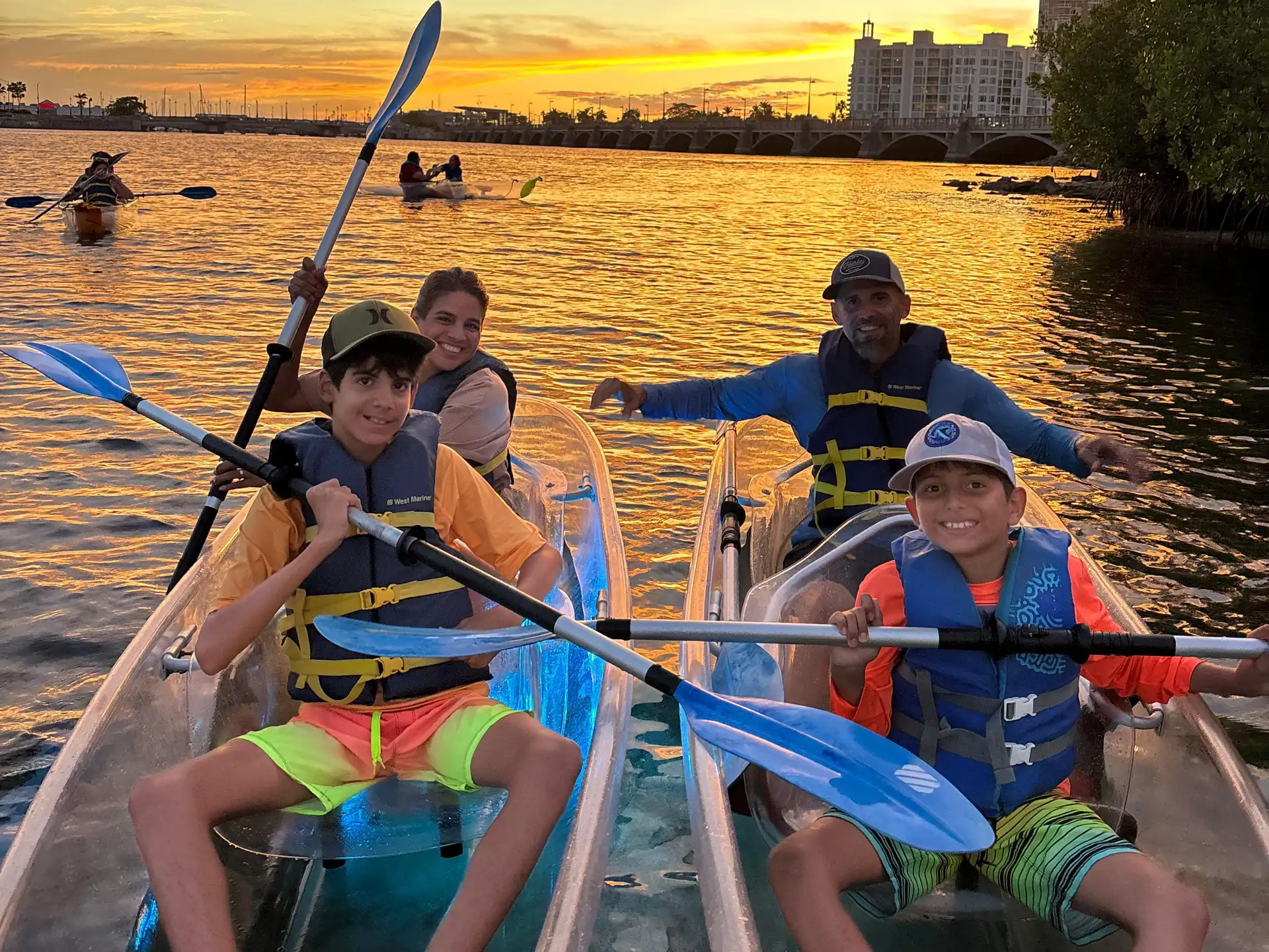 Family kayaking on a lake during a vibrant sunset, wearing life vests.