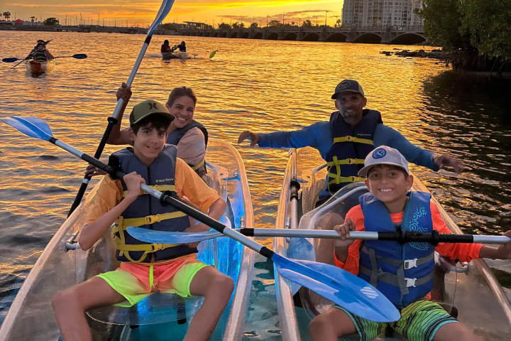 Family kayaking on a lake during a vibrant sunset, wearing life vests.