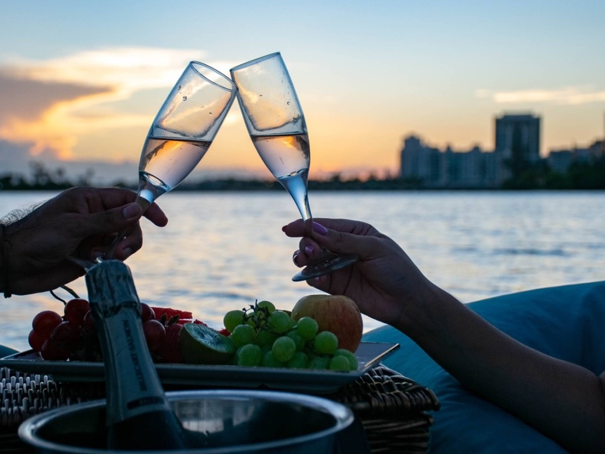 Two people clinking champagne glasses on a waterfront at sunset.