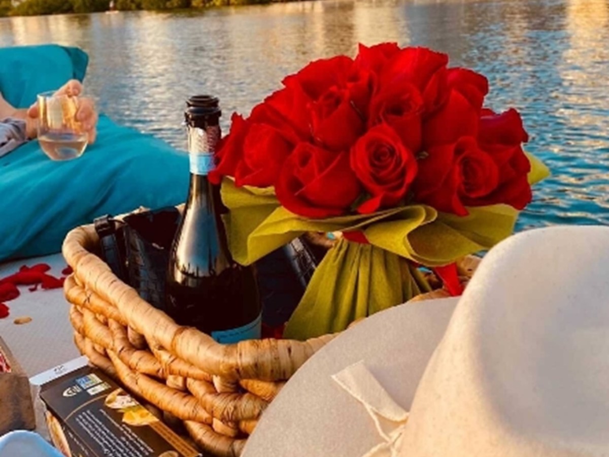 Picnic basket with wine and roses on a boat, cityscape view.