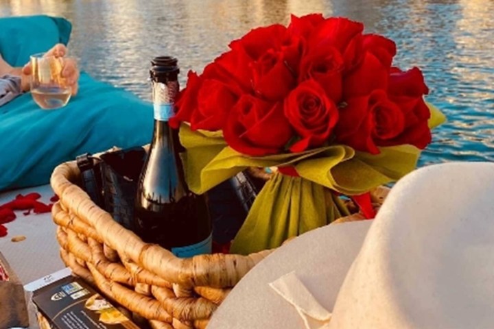 Picnic basket with wine and roses on a boat, cityscape view.