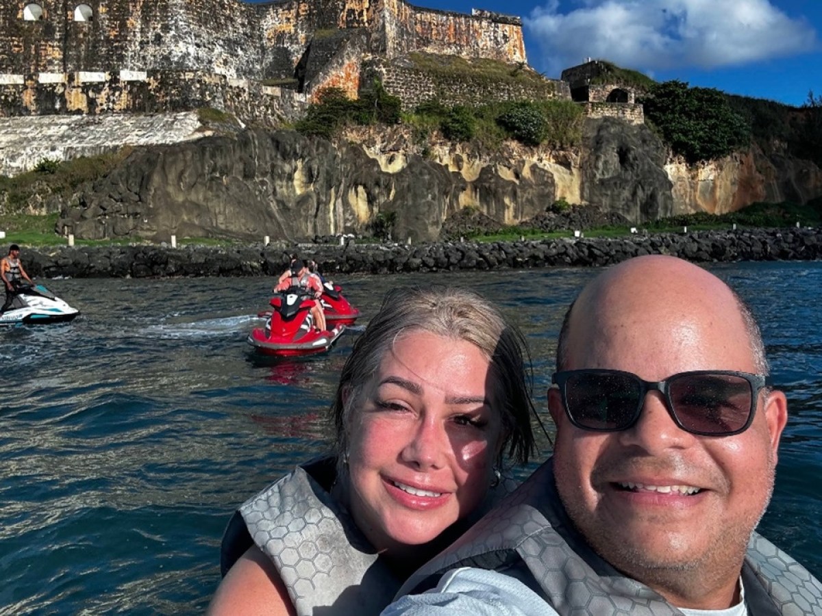 Two people smiling on jet skis with a historic fort in the background.