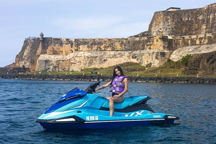 Person on a blue jet ski near a historic fortress by the sea.