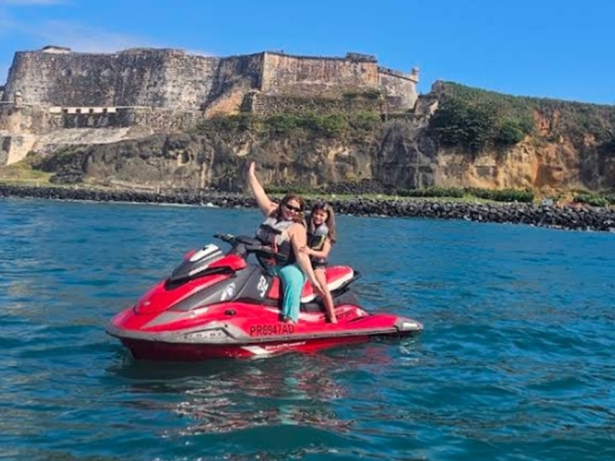 Two people on a red jet ski in front of a coastal fortress.