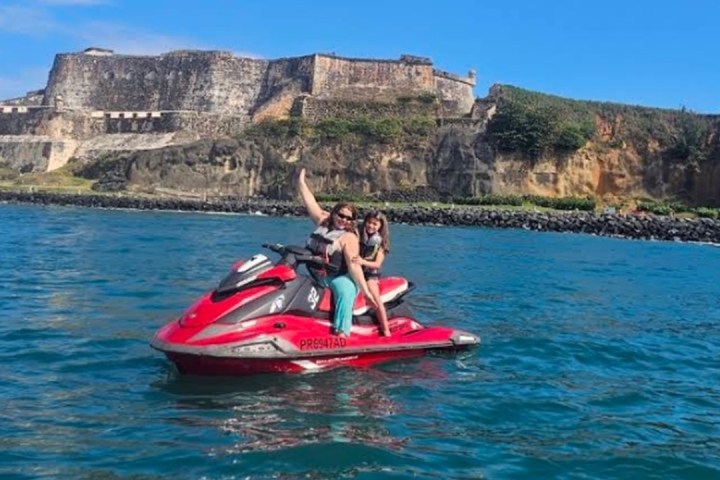 Two people on a red jet ski in front of a coastal fortress.
