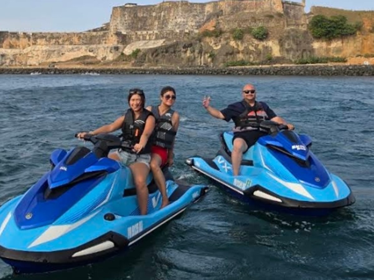 Three people on jet skis in front of a large stone fortress.