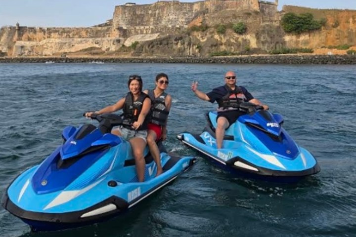 Three people on jet skis in front of a large stone fortress.