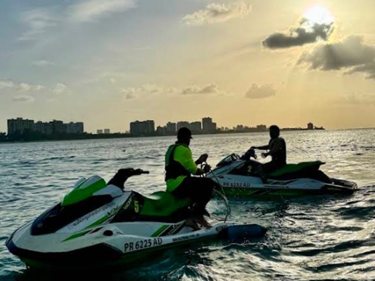 Two people on jet skis at sunset near a city skyline.