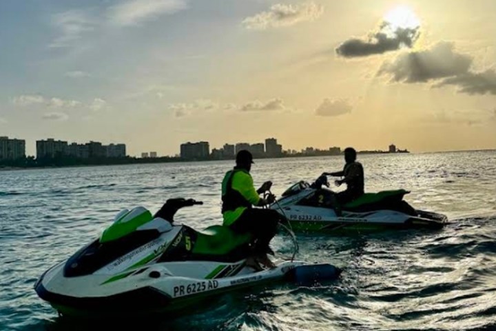 Two people on jet skis at sunset near a city skyline.
