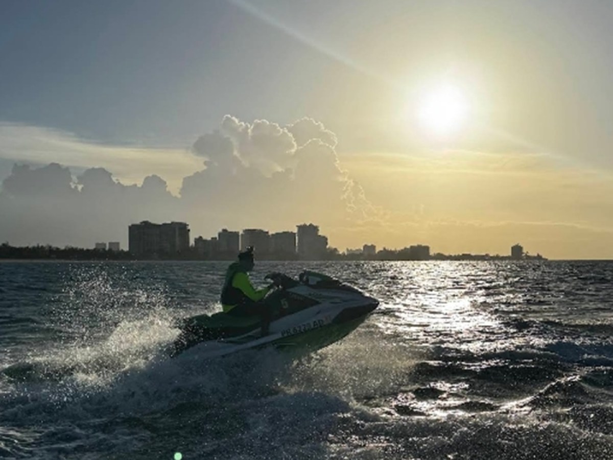 Person riding a jet ski on ocean at sunset with city skyline in the background.