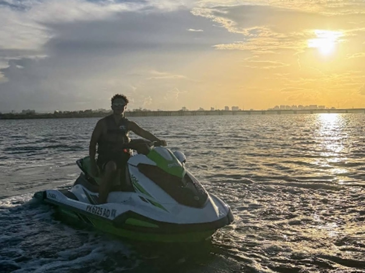 Person on jet ski in ocean at sunset with city skyline in background.