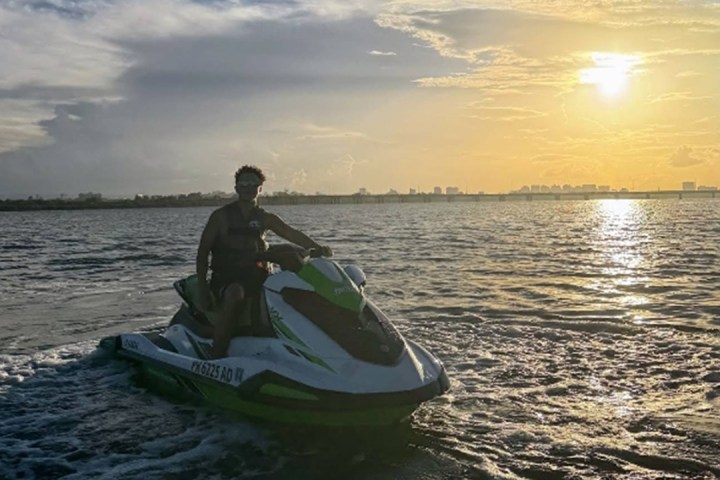 Person on jet ski in ocean at sunset with city skyline in background.