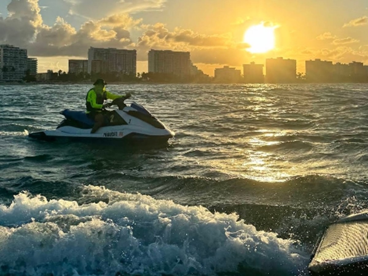 Person jet skiing at sunset near a city skyline on the ocean.