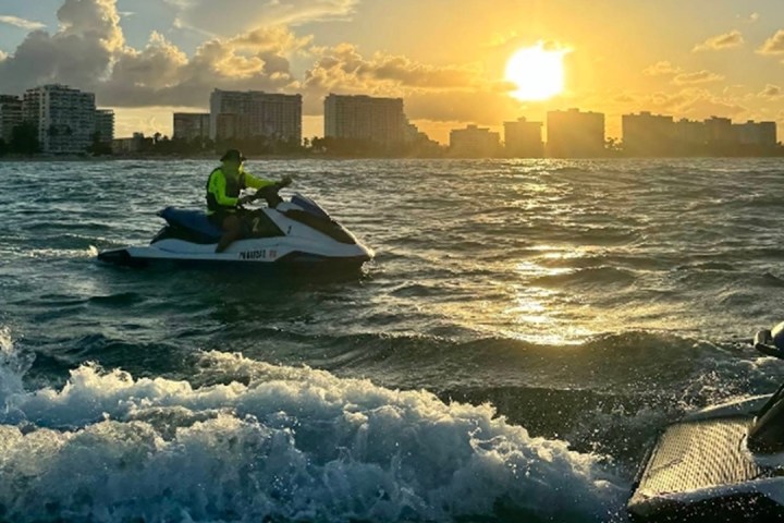 Person jet skiing at sunset near a city skyline on the ocean.