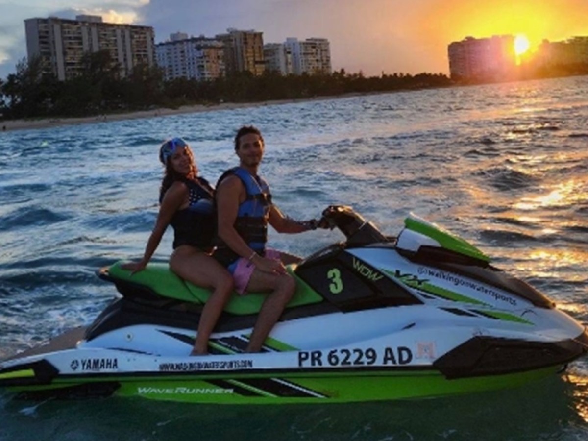 Two people on a jet ski at sunset on the ocean near a city skyline.