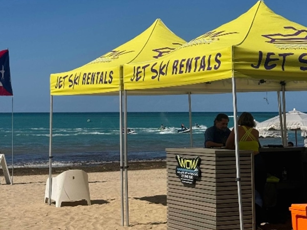 Beach with yellow jet ski rental tents and a flag waving.