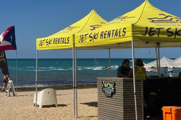 Beach with yellow jet ski rental tents and a flag waving.