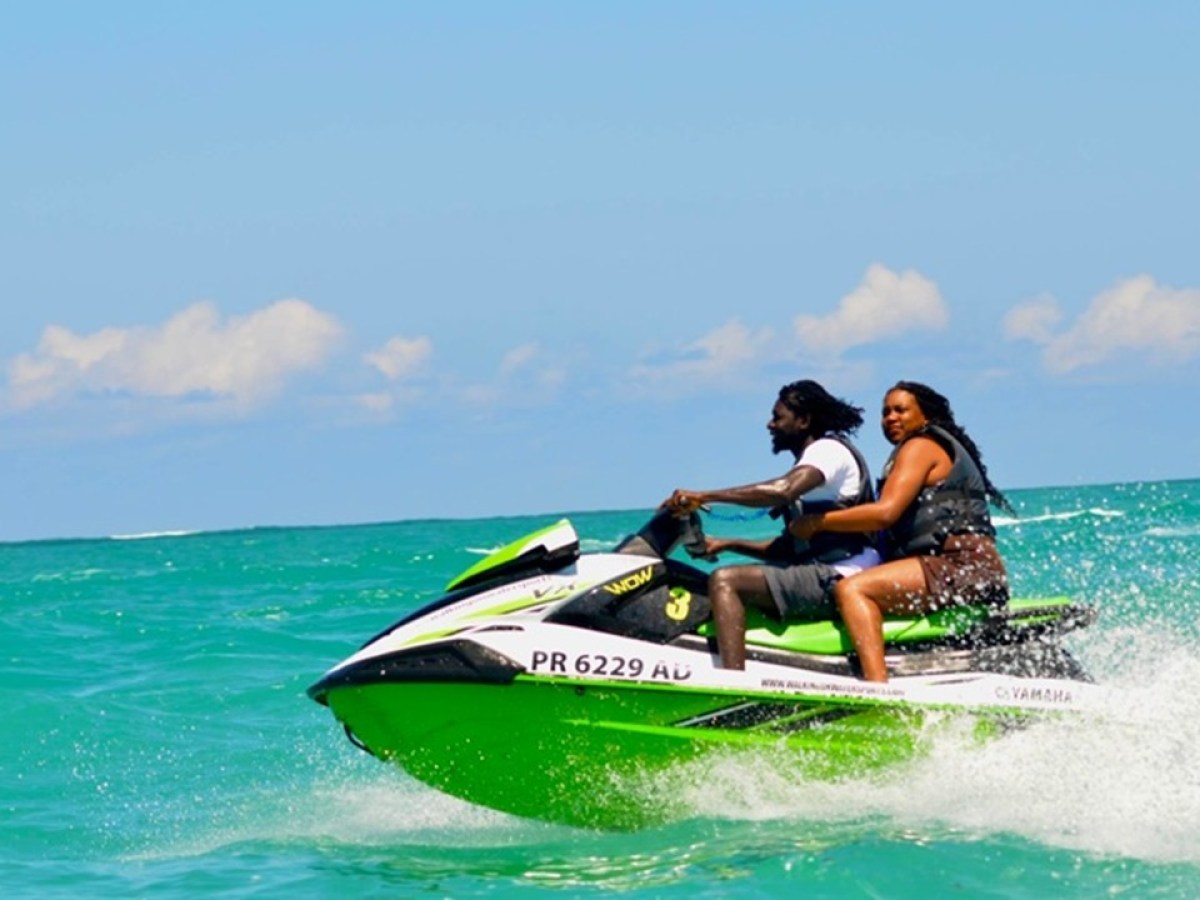 Two people riding a green jet ski on the ocean under a clear blue sky.