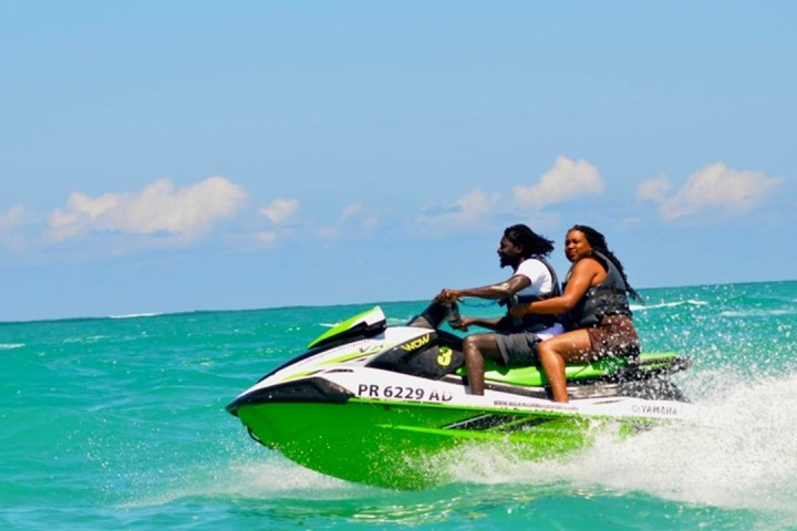 Two people riding a green jet ski on the ocean under a clear blue sky.