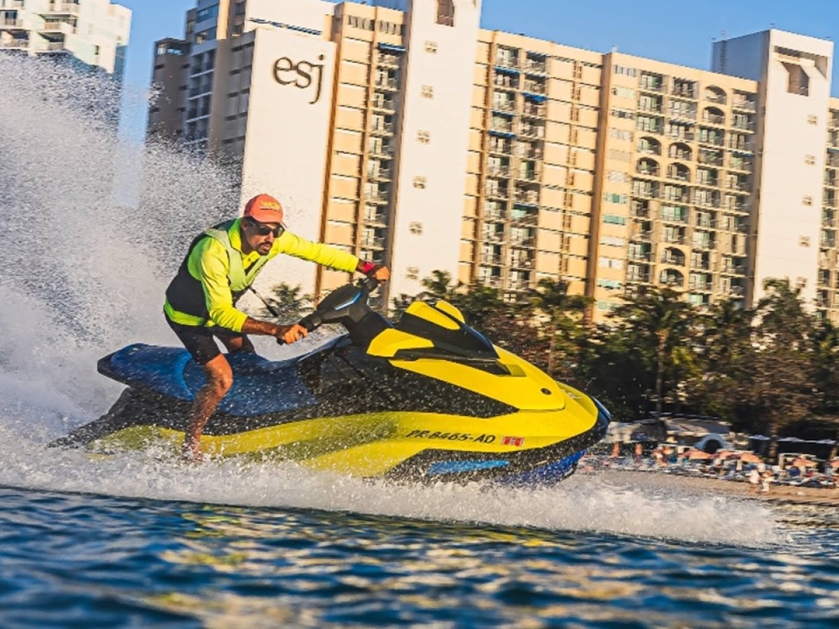 Person in yellow jacket riding a yellow jet ski near a beachfront building.