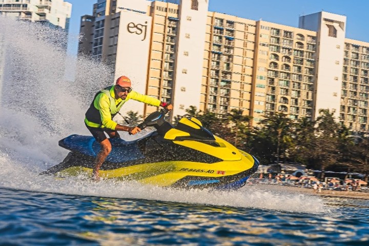 Person in yellow jacket riding a yellow jet ski near a beachfront building.